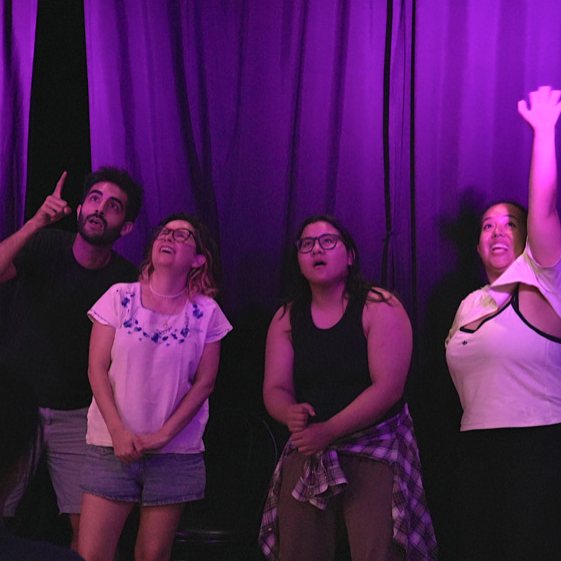Four players mid-scene at a Potluck jam, one arm thrown to the sky, everyone laughing